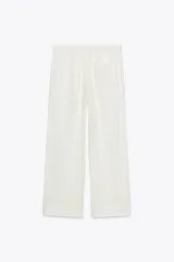 Pantalón blanco de lino con tiro medio, cintura ajustable con cordones, bolsillos laterales ocultos y detalle de entredós combinados a tono.