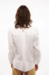 Camisa blanca de lino con corte clásico, cuello camisero, mangas largas con puños abotonados y volados en los hombros.