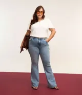 Pantalón de jean azul claro, modelo flare, con cintura elástica, trabillas para cinturón, bolsillos delanteros y traseros, y botón en forma de flor.