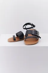 Sandalia plana de cuero en tonos marrón y negro, con detalle de hebilla en el tobillo y diseño minimalista.