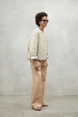 Chaqueta color crema con cuello redondo y cierre frontal con botones a presión.