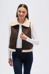 Chaleco sin mangas de eco-cuero marrón con forro y cuello de piel sintética color crema. Presenta cierre frontal y detalles de hebillas ajustables en los laterales.