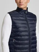 Chaleco acolchado azul marino de nailon reciclado, con cuello alto, cierre de cremallera, bolsillos laterales y logo de Tommy Hilfiger bordado en el pecho.