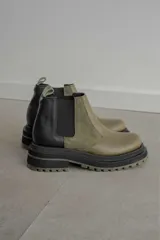 Botines Chelsea de cuero color verde oliva y negro, con elásticos laterales negros, tirador trasero y suela track de goma color verde oliva.