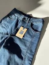 Pantalón de jean de tiro alto, corte flare, color azul oscuro, con costuras frontales y detalle desflecado en el ruedo.
