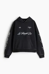 Sudadera tipo canguro de algodón pesado con efecto lavado oscuro, corte oversized y hombros caídos. Presenta estampado frontal en blanco con texto cursivo "Le Strade Di MMXXVI", dos banderas a cuadros, texto pequeño en la parte superior derecha y texto vertical en la manga izquierda. La manga derecha tiene un patrón de estrellas delineadas.