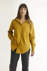 Camisa color mostaza de corte clásico, con cuello camisero, manga larga, cierre frontal con botones y bolsillo de parche en el pecho.