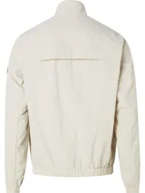 Campera Calvin Klein color beige claro, confeccionada en nailon arrugado reciclado. Tiene cuello alto, puños y bajo elásticos, cierre con cremallera, bolsillos con cremallera en la cintura, abertura de ventilación en la espalda, forro de poliéster reciclado e insignia con el logo de goma de Calvin Klein en la manga.