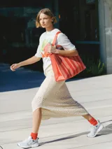 Bolso tipo tote de tela color crema con rayas verticales rojas. Tiene doble asa de hombro y correa larga para usar cruzado.