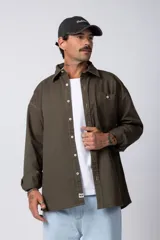Camisa verde militar de manga larga, corte oversize, con cuello clásico, cierre frontal con botones y bolsillo en el pecho. Confeccionada en algodón suave y con costuras a la vista.
