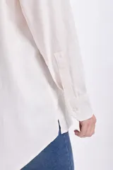 Camisa blanca de lino de manga larga con cuello clásico, cierre frontal con botones y bolsillo en el pecho.