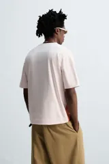 Camiseta color crema de corte holgado con cuello redondo y mangas cortas. Estampado frontal con la ilustración de un hombre sentado en un sillón.