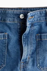 Pantalón de jean de algodón con leve stretch, tiro alto y pierna ancha. Presenta bolsillos de parche cuadrados en la parte delantera y bolsillos traseros. El lavado es celeste medio con efecto de desgaste vertical en las piernas.