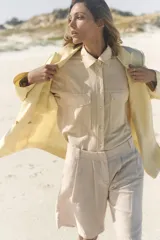 Blazer color crema confeccionado en hilatura con lino, de corte recto, con cuello solapa de muescas y manga larga acabada en abertura y botones. Tiene bolsillos delanteros y cierre frontal cruzado con botones.