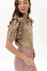 Camisa de lino color lila con volados en el cuello y en las mangas cortas abullonadas. Presenta un diseño de corte recto con cierre frontal de botones.