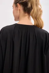 Vestido corto negro con cuello mao, abotonadura parcial y mangas largas abullonadas.