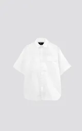 Camisa blanca de manga corta confeccionada en poplin de algodón, con silueta oversize y dos bolsillos delanteros, uno con solapa y otro con ojal y botón.