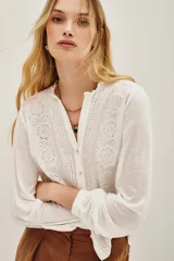 Camisa blanca de manga larga con cuello mao y escote en V. Presenta detalles de bordado calado en el frente y las mangas.