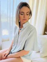 Camisa celeste de lino con mangas cortas, botones de lino y detalle drapeado en la espalda.