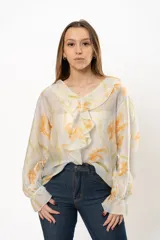 Blusa blanca traslúcida con estampado floral color naranja, cuello con volados y mangas largas abullonadas con puños elásticos.