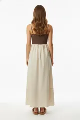 Vestido largo con breteles finos, cuerpo superior color marrón y falda larga color beige. El cuerpo superior es ajustado y la falda es amplia y con caída.