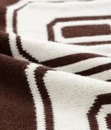 Remera oversized deportiva color marrón con cuello en V, rayas blancas en las mangas y en la parte inferior, y el número "62" estampado en blanco en el frente. Incluye el bordado "Humanity" y un logo de globo terráqueo.