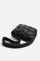 Bandolera negra acolchada de tejido técnico con cierre de cremallera. Tiene dos bolsillos interiores, uno con cremallera. El asa de hombro es ajustable.