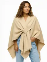 Ruana de tejido soft color beige, con cuello en V y un lazo o pasador frontal para ajustar. El ruedo tiene terminación desflecada.