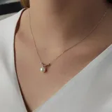 Conjunto de collar y aros en plata 925 con perlas de río. El collar tiene una cadena fina de plata con una perla central y pequeñas cuentas plateadas. Los aros son colgantes con una perla cada uno.