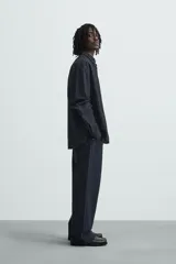 Camisa negra con finas rayas verticales blancas, de corte holgado, manga larga y cuello abotonado.