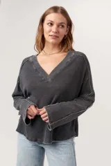Remera de manga larga con escote en V amplio, confeccionada en tejido térmico suave con lavado burnout que le da un acabado vintage. Presenta costuras expuestas y bordes sin rematar, con mangas levemente acampanadas.