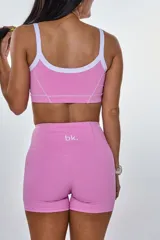 Conjunto deportivo rosa compuesto por un top con tirantes blancos y un short ajustado con costuras blancas.