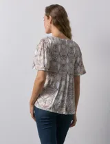 Blusa de tejido elastizado con estampado geométrico en tonos beige y blanco. Tiene cuello redondo con escote en V y lazo de ajuste, y mangas cortas amplias. Marca Cupio.