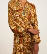 Vestido midi de viscosa con estampado de follaje en tonos marrones y verdes. Tiene cuello en V, cierre frontal con botones, mangas largas con elástico en los puños y corte evasé.