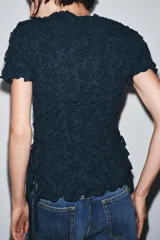 Top negro de punto con textura arrugada, cuello redondo, mangas cortas y lazos laterales.