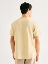 Camiseta blanca de algodón con cuello redondo y mangas cortas. Estampa rectangular con borde negro que contiene la frase "NATURAL ATMOSPHERE" en letras mayúsculas y una imagen de montañas y mar.