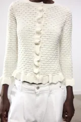 Chaqueta de punto amarilla con cuello redondo, manga larga y cierre frontal con botones. Detalle de volantes en los bordes.