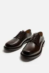 Zapato de vestir tipo derby, color marrón oscuro, con cordones, capellada de cuero brillante, forro y plantilla de cuero y suela plana.