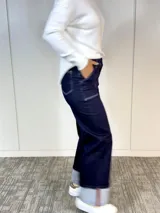Pantalón de jean azul oscuro, de corte ancho, con bolsillos delanteros y traseros, y dobladillo ancho en el ruedo.