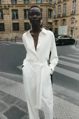 Camisa blanca de satén con cuello solapa y manga larga. Cierre frontal con botones dorados.