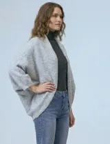 Cardigan negro de tejido suave, estilo poncho o capa, con cuello tipo chal y mangas amplias.