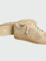 Championes Golden Goose modelo Ball Star confeccionados en gamuza color beige. Presentan una capellada con perforaciones decorativas, cierre de cordones al tono y el icónico logo de estrella en el lateral. La suela de goma incluye un detalle de costura visible en todo el contorno.