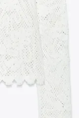 Top blanco de encaje con bordados florales, cuello redondo y mangas largas.