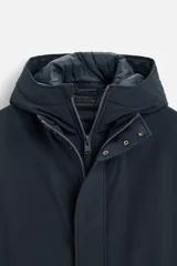 Parka azul marino de tejido técnico repelente al agua, corte regular fit, interior acolchado, cuello alto con capucha, mangas largas con puños de rib, cuello interior desmontable con cremallera, bolsillos de vivo en cadera y bolsillo interior. Cierre frontal con cremallera oculta por solapa con botones a presión.