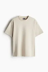 Remera color beige de corte holgado, cuello redondo y mangas cortas.