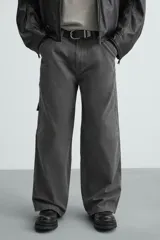 Pantalón de algodón color gris oscuro con efecto lavado, corte relaxed fit y pierna ancha. Presenta bolsillos delanteros, bolsillos traseros de plastrón y un bolsillo lateral con cierre de cremallera en la pierna.