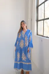 Vestido largo celeste con estampado floral en beige, corte evasé, cuello camisero, mangas largas con volados y falda escalonada.