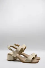 Sandalias de cuero color beige con taco cuadrado y tira ancha sobre los dedos. Presenta pulsera al tobillo con hebilla dorada.