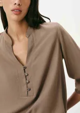 Blusa color verde claro, de mangas 3/4 con elástico en los puños, escote en V con botones y corte holgado.