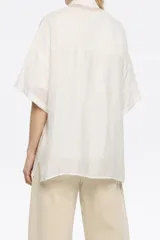 Camisa oversize blanca con rayas verticales finas en gris oscuro, cuello camisero, manga corta ancha, cierre frontal con botones y bolsillo de parche en el pecho. Confeccionada en viscosa y poliamida.
